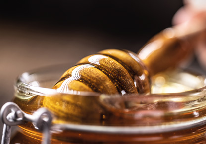 A utensil is dipped into a small glass ramekin of honey.